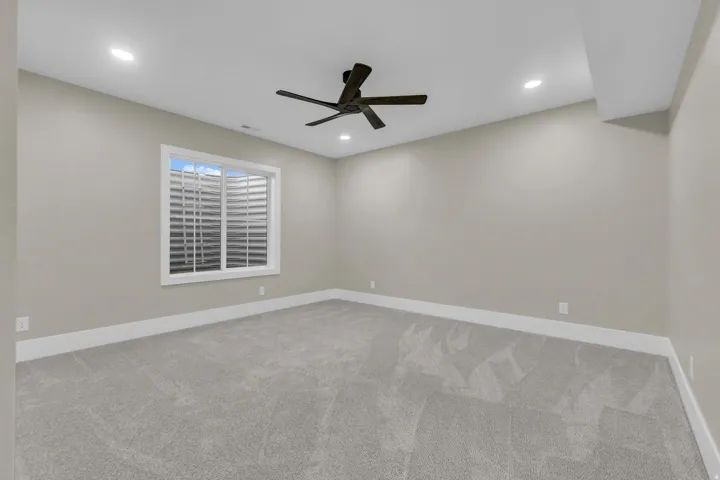 Carpeted room featuring a ceiling fan, recessed lighting, and a white-framed window with a window well