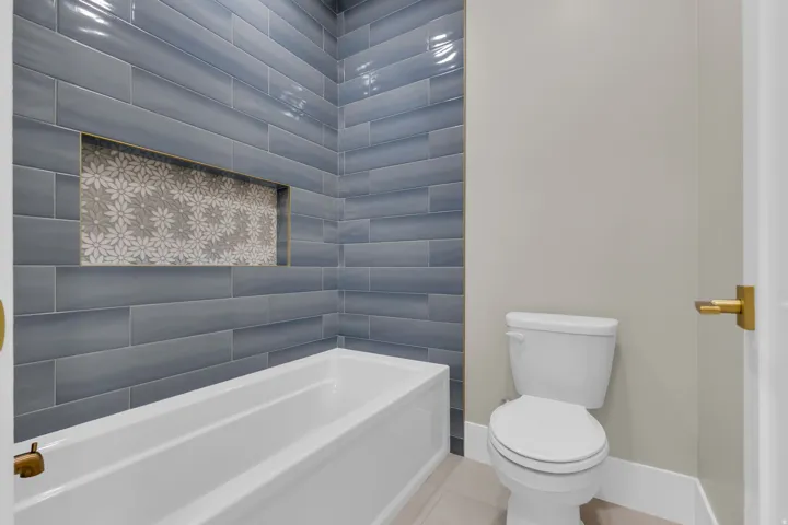 Bathtub with blue subway tile surround featuring a decorative mosaic niche