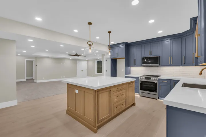 Contemporary kitchen featuring blue shaker-style cabinetry, a light wood-finish island with a white countertop, and stainless steel appliances