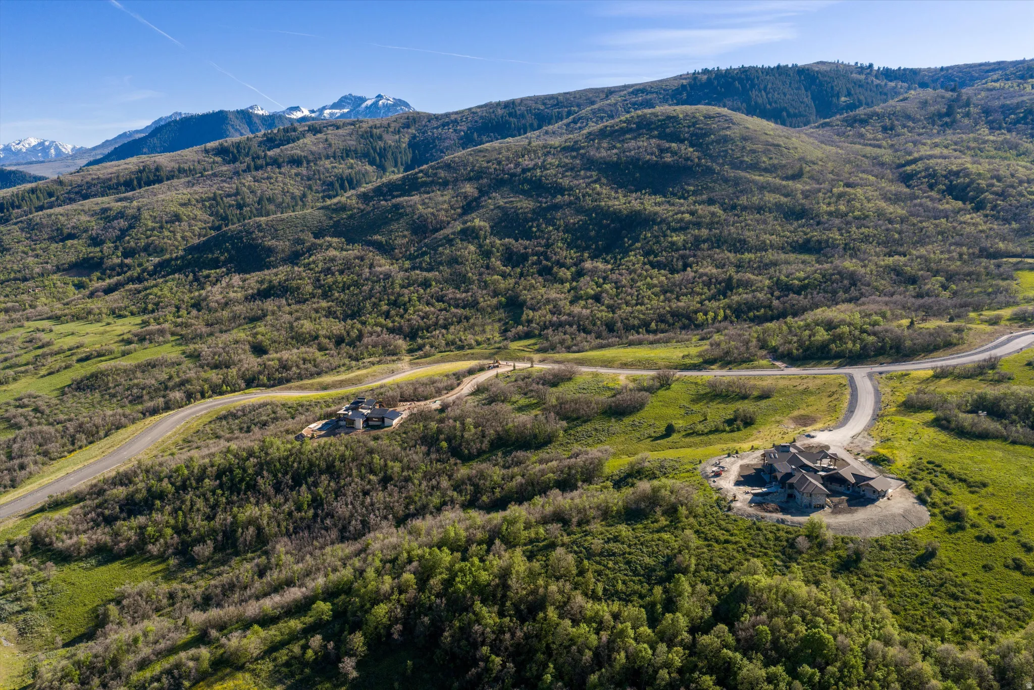 Mountainous terrain featuring two distinct residences surrounded by lush green foliage and winding roadways