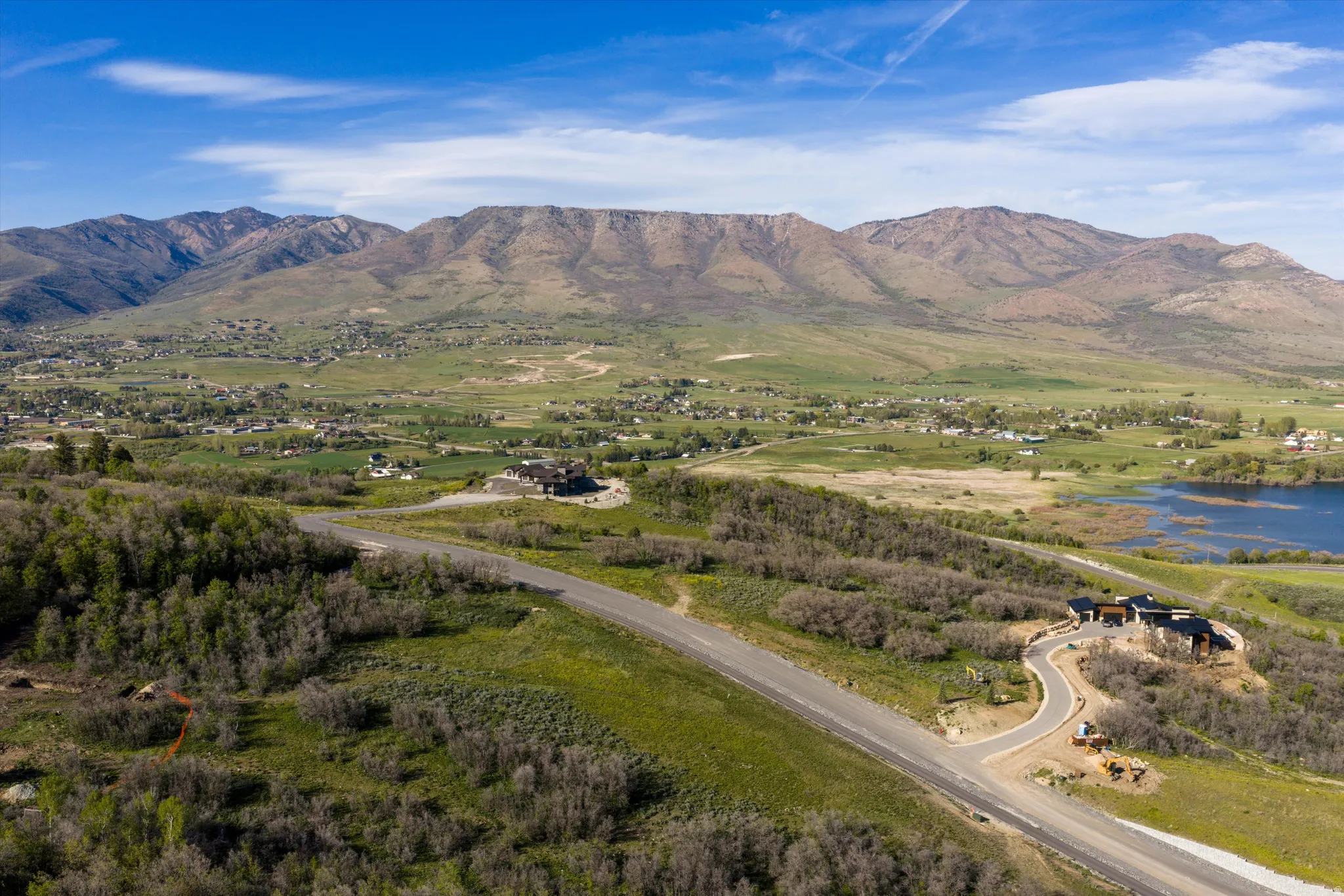Expansive mountain landscape with a visible lake, winding paved roads, and a cluster of residences