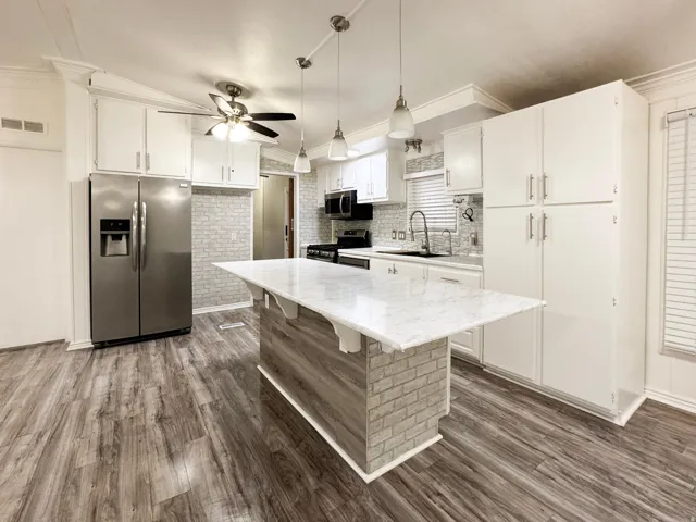 Kitchen featuring a central island with a white surface, track lighting, wood-finish flooring, white cabinetry, and stainless steel appliances