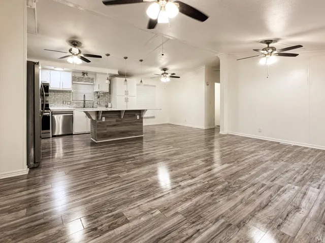 Open-concept living space featuring wood-finish flooring, a kitchen island with seating, stainless steel appliances, white cabinetry, and multiple ceiling fans