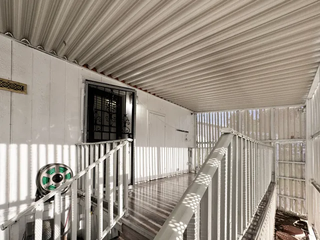 Covered porch entryway with white siding, metal security door, and wood-finish flooring