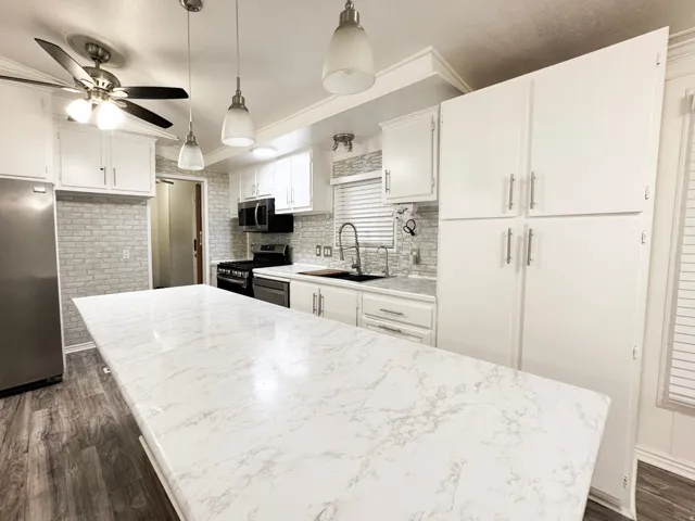 Spacious kitchen featuring an extended island with a white marble-patterned countertop, white cabinetry with brushed nickel hardware, and grey brick-patterned tile backsplash