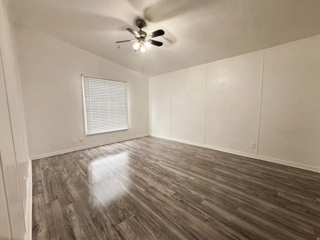 Spacious Bedroom 1 featuring wood-finish flooring, white paneled walls, and a window with horizontal blinds