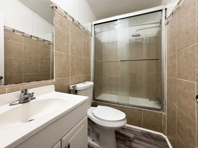 Bathroom featuring a single vanity, wood-finish flooring, tiled walls, and a shower with a sliding glass enclosure