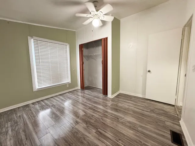 Bedroom 2 with wood-finish flooring, a ceiling fan, window with blinds, and an open closet with shelving