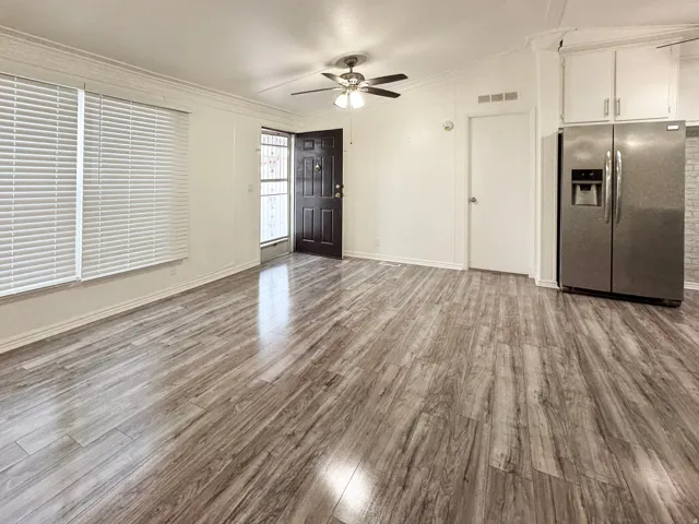 Open-concept living space featuring wood-finish flooring, white horizontal blinds, and a dark wood-finish entry door with a security screen