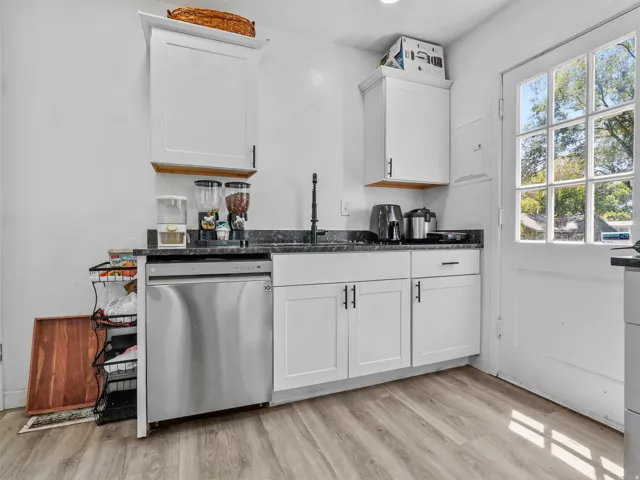 Kitchen area featuring shaker-style white cabinetry with matte black hardware, dark stone-finish countertops, a stainless steel dishwasher, and wood-finish flooring
