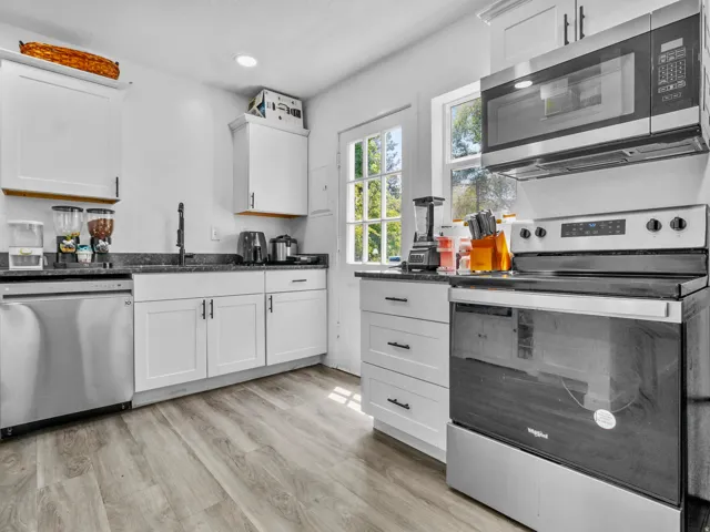 Modern kitchen featuring white shaker cabinetry, dark countertops, stainless steel appliances including a dishwasher, oven, and microwave, and wood-finish flooring