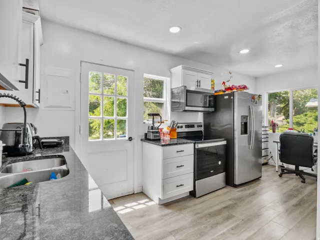 Kitchen featuring wood-finish flooring, white cabinetry with black hardware, stainless steel appliances, dark stone countertops, and recessed lighting