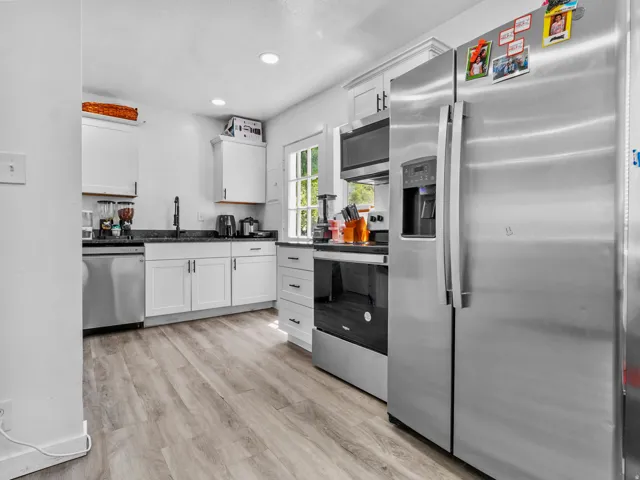 Kitchen featuring stainless steel appliances, white cabinetry, dark countertops, and wood-finish flooring