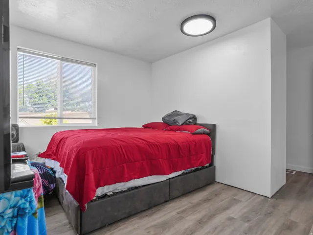 Bedroom featuring wood-finish flooring, a contemporary flush-mount ceiling light, and a window with blinds