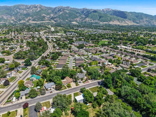 Expansive suburban landscape featuring established residential neighborhoods, mature trees, a prominent paved road system, and distant snow-capped mountains