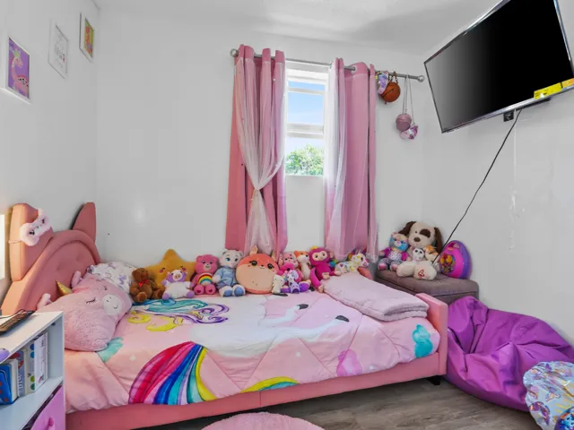 Room featuring a window with pink draperies, a wall-mounted television, and wood-finish flooring
