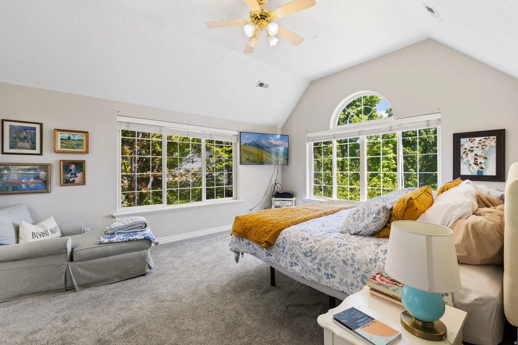 Primary bedroom with vaulted ceiling, featuring expansive windows, an arched transom window, and ceiling fan