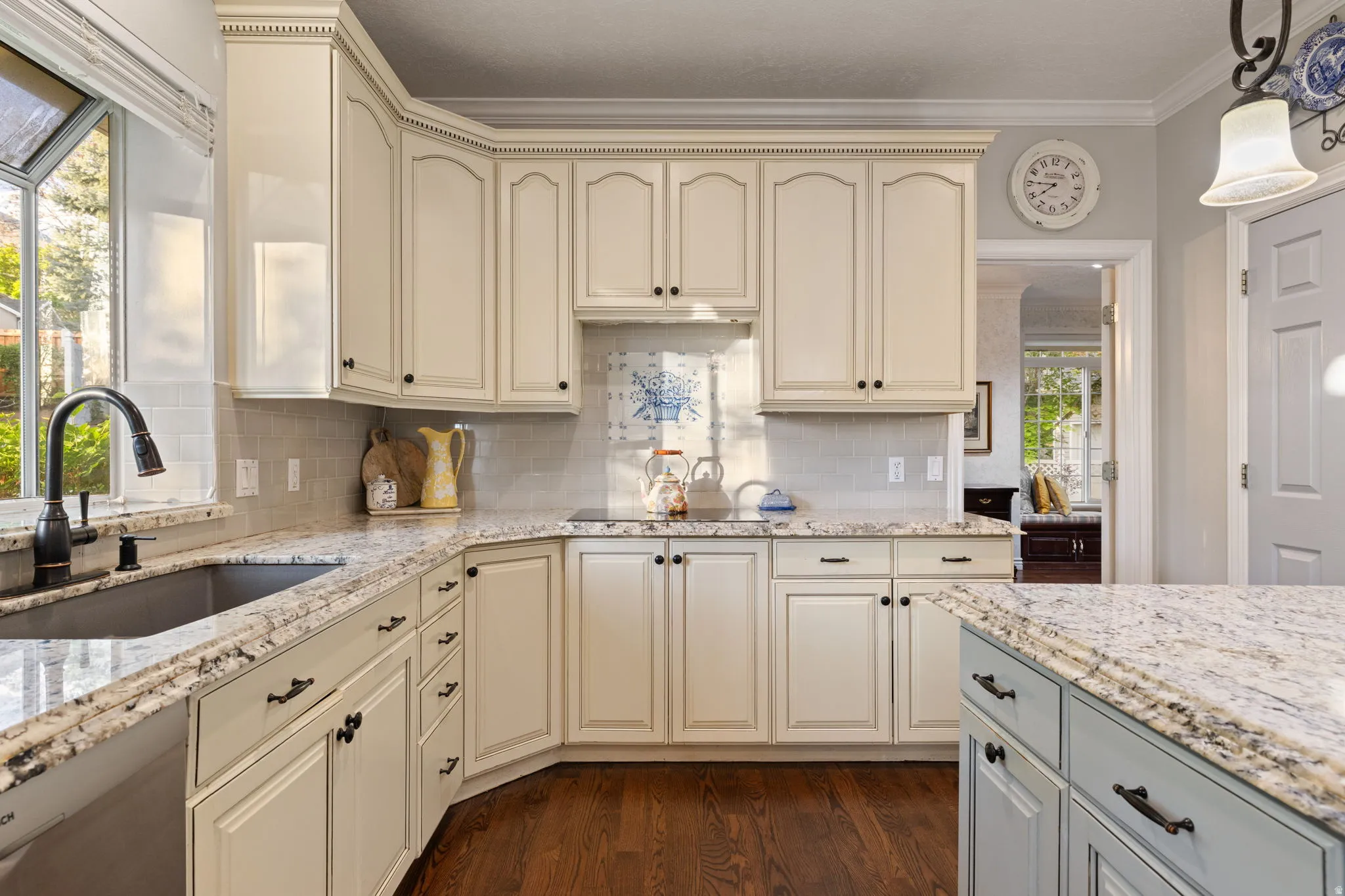 Kitchen featuring white cabinetry, granite countertops, an undermount sink with a gooseneck faucet, a tile backsplash, and wood flooring