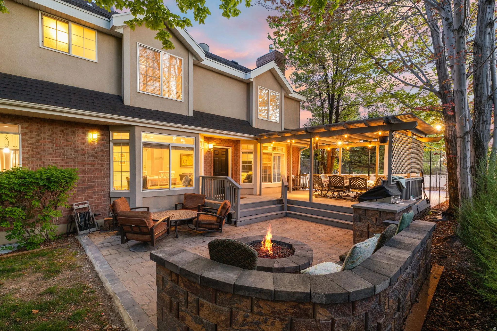 Spacious backyard featuring a paver patio with a built-in fire pit, stone-clad seating, and a covered outdoor deck
