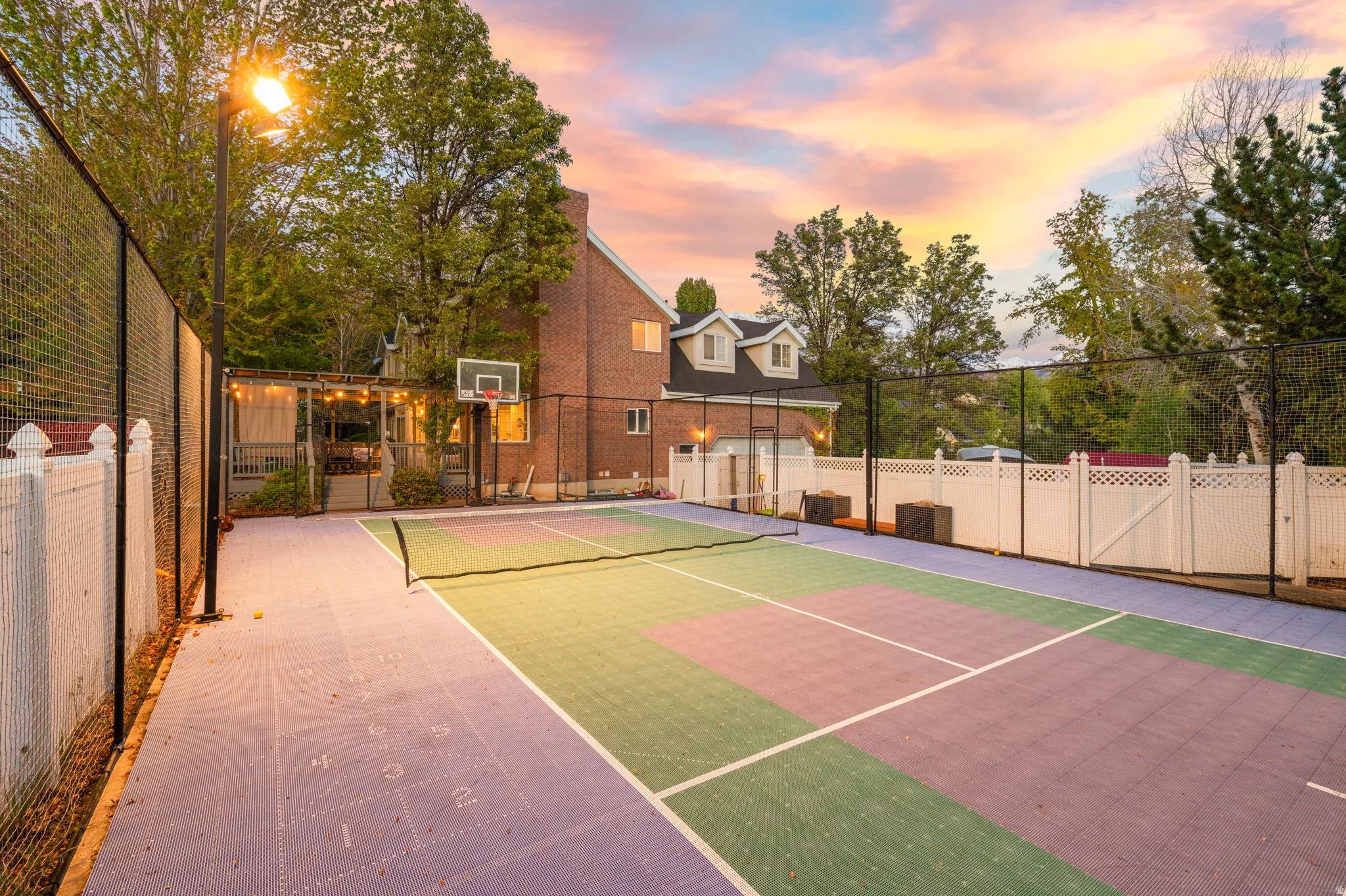 Multi-sport court featuring vibrant purple and green surfacing, integrated shuffleboard lines, a basketball hoop, and perimeter fencing