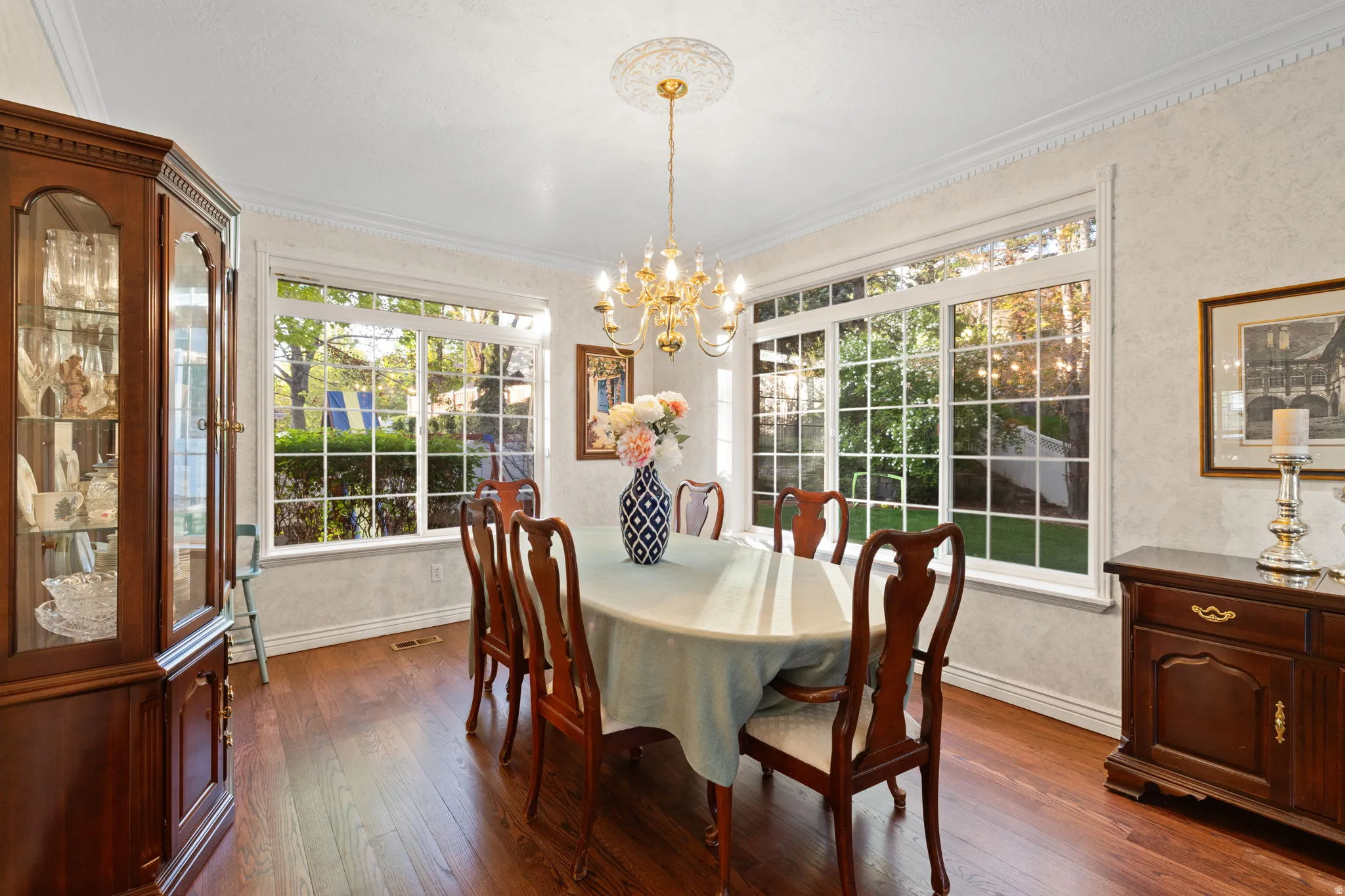 Dining space featuring two large multi-pane windows with white trim, dark wood-finish flooring, crown molding, and a chandelier with a decorative ceiling medallion