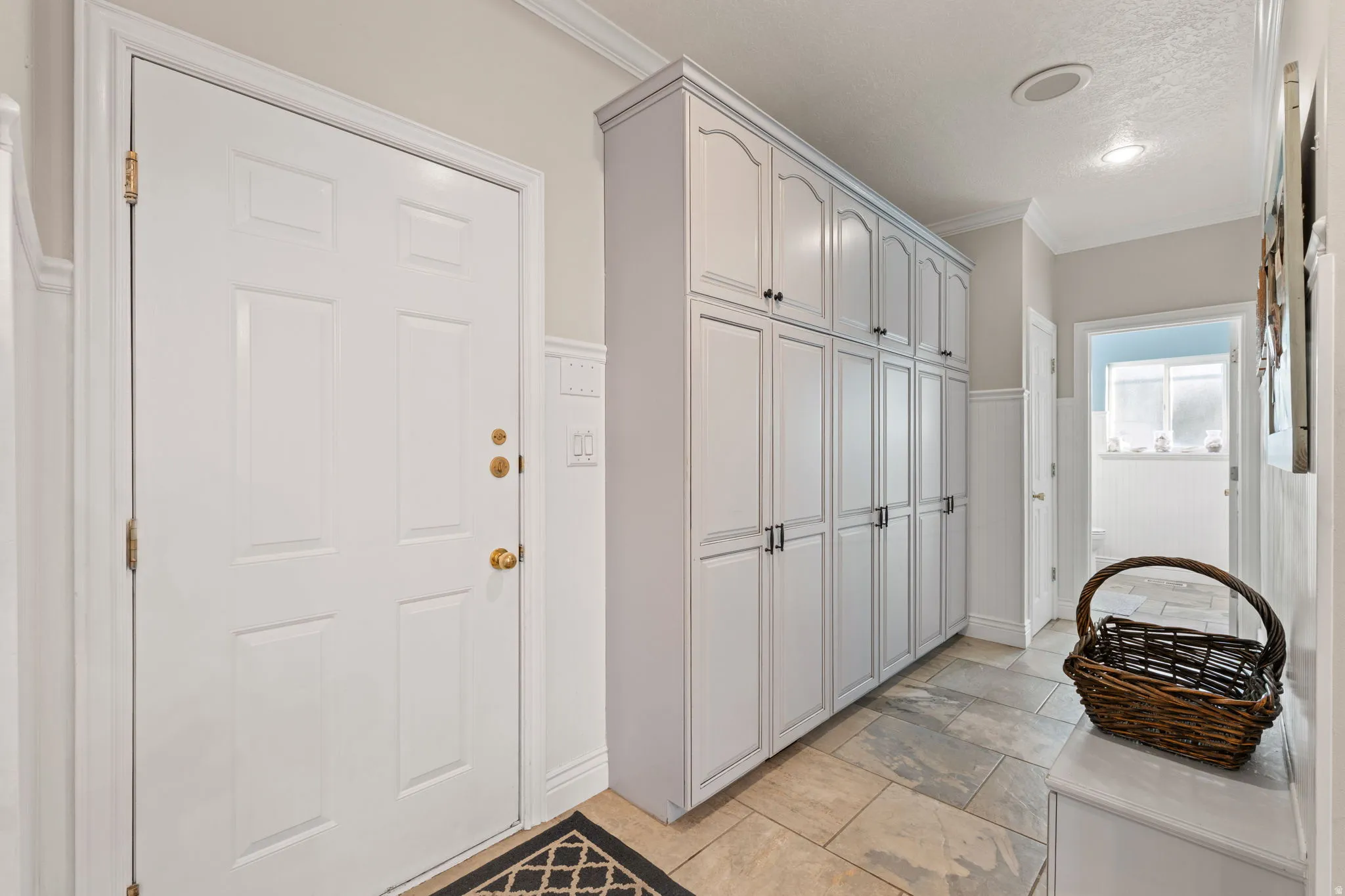 Entryway from garage with extensive built-in cabinetry with dark hardware, and large tile flooring