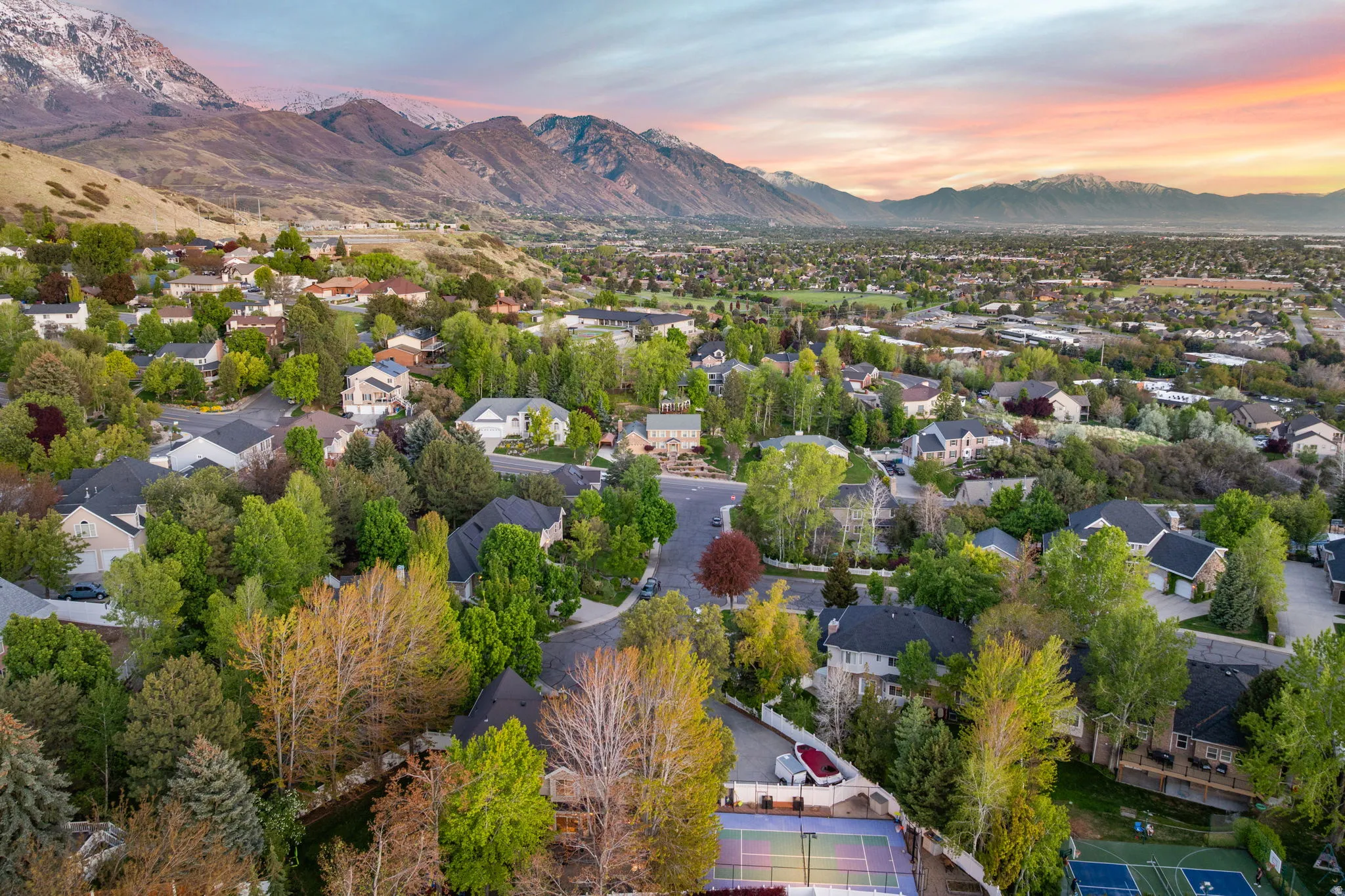 Residential neighborhood featuring mature trees, diverse home architecture, paved streets, and mountainous terrain