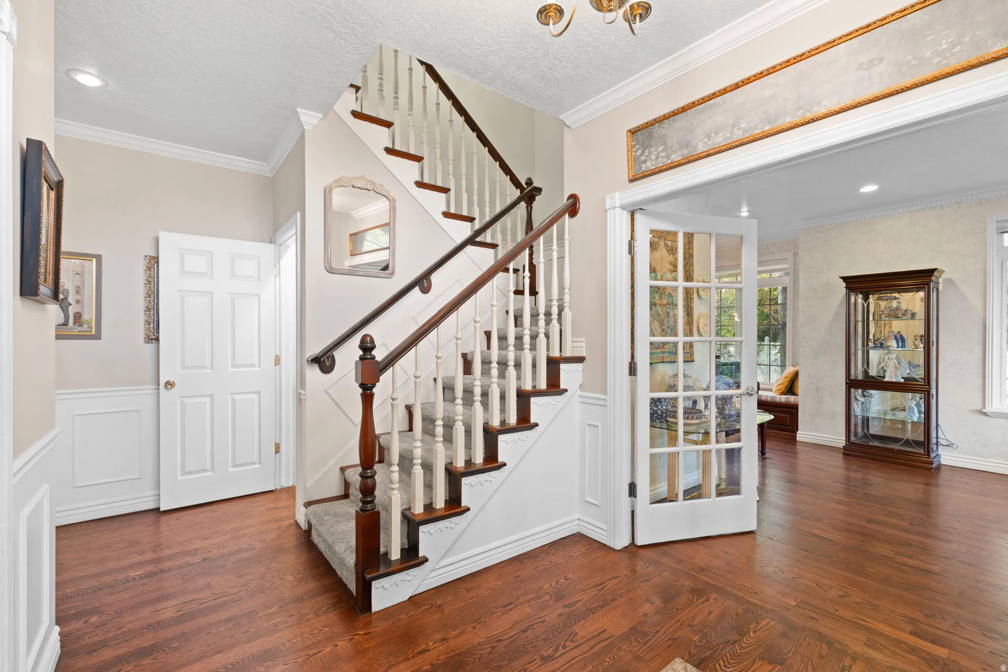 Grand staircase with carpeted treads and wood banister, featuring wainscoting and crown molding
