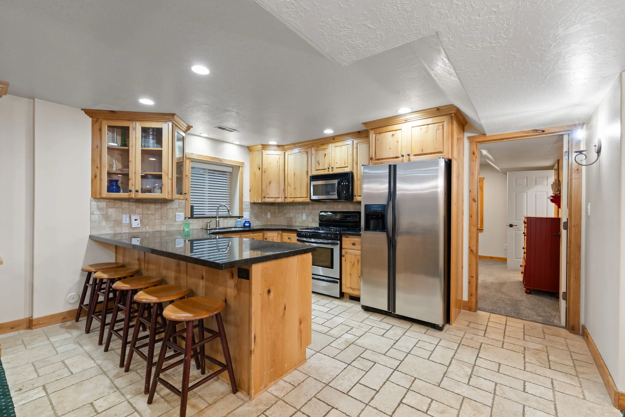 Basement kitchen featuring natural wood cabinetry, granite countertops, tiled flooring, and stainless steel appliances