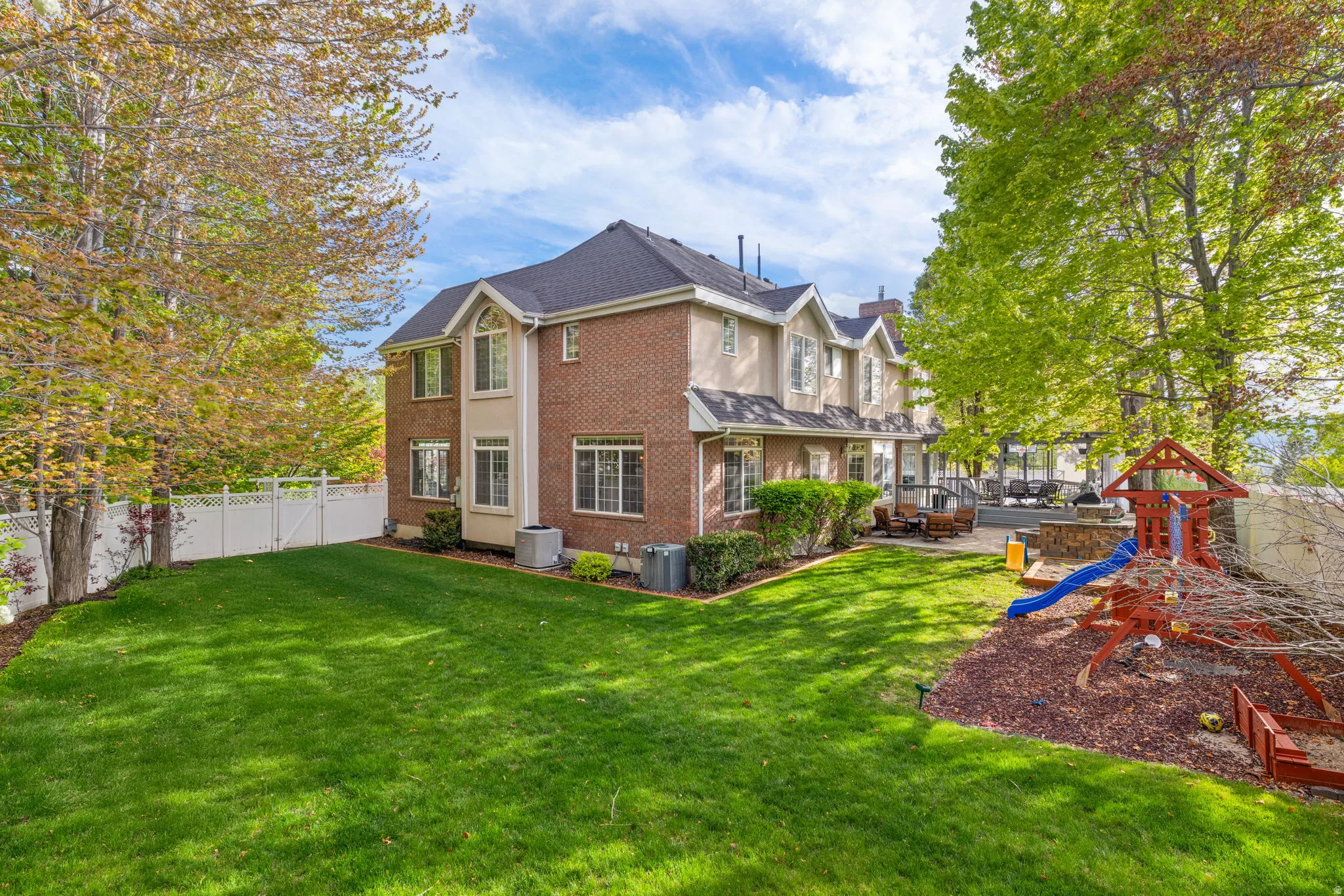 Expansive backyard featuring a manicured lawn, white vinyl fencing, and mature trees