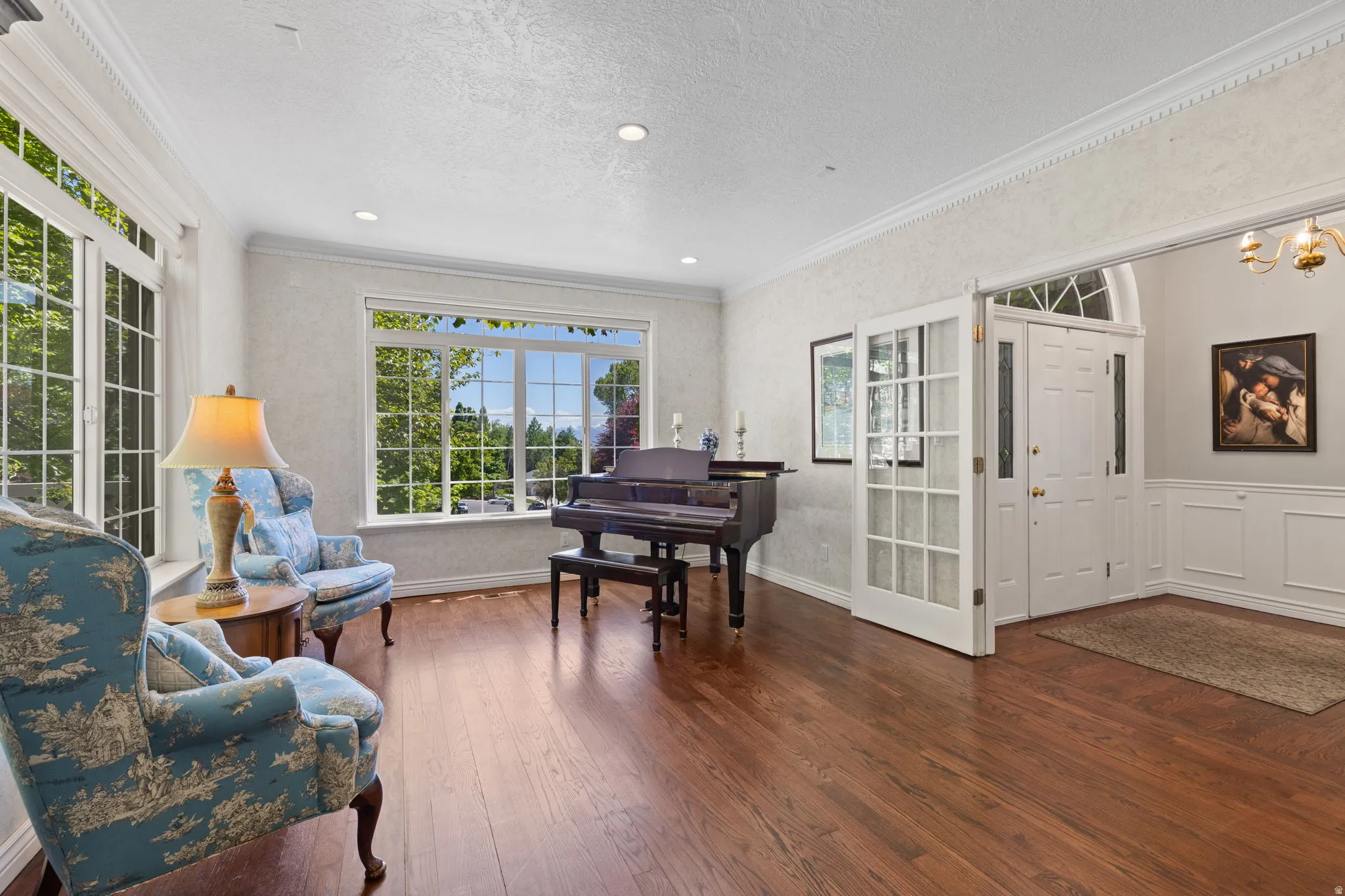 Spacious sitting room featuring wood-finish flooring, extensive window grid detailing, crown molding, and wainscoting