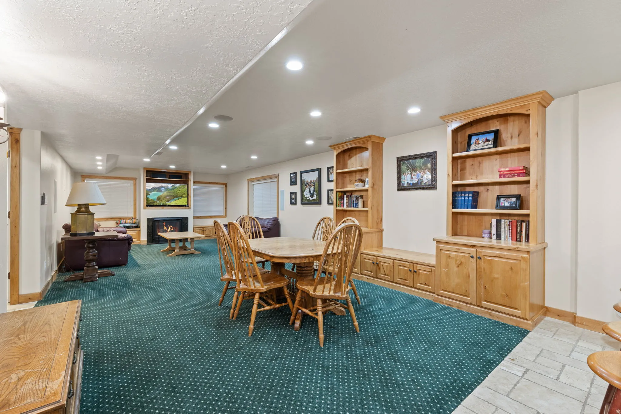 Spacious room featuring recessed lighting, built-in wooden shelving with lower cabinetry, and a fireplace with a mounted television
