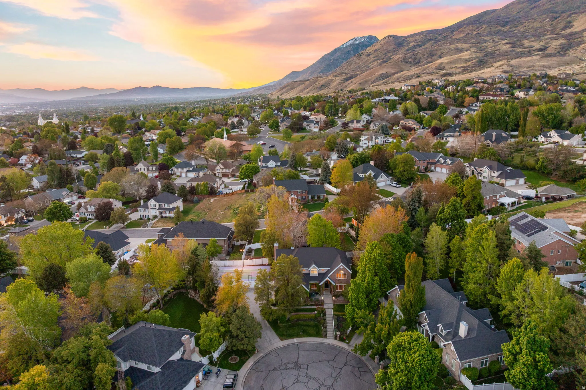Residential neighborhood with diverse home styles, mature landscaping, tree-lined streets, and mountain backdrop