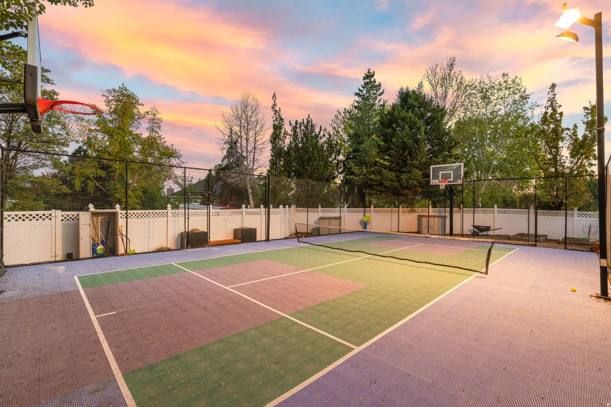 Multi-sport court featuring vibrant purple and green surfacing, integrated shuffleboard lines, a basketball hoop, and perimeter fencing