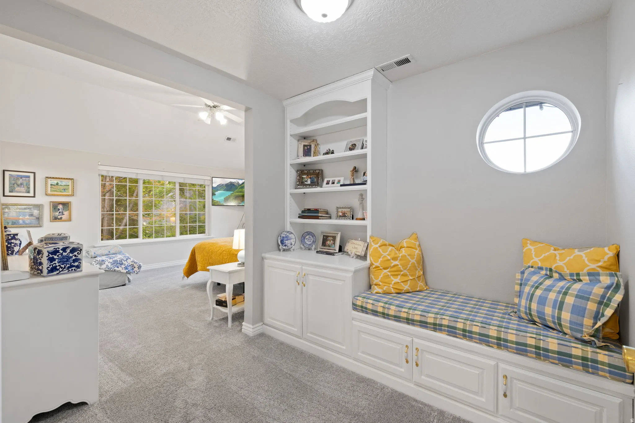 Primary bedroom with built-in window seat with storage cabinetry and an oval window