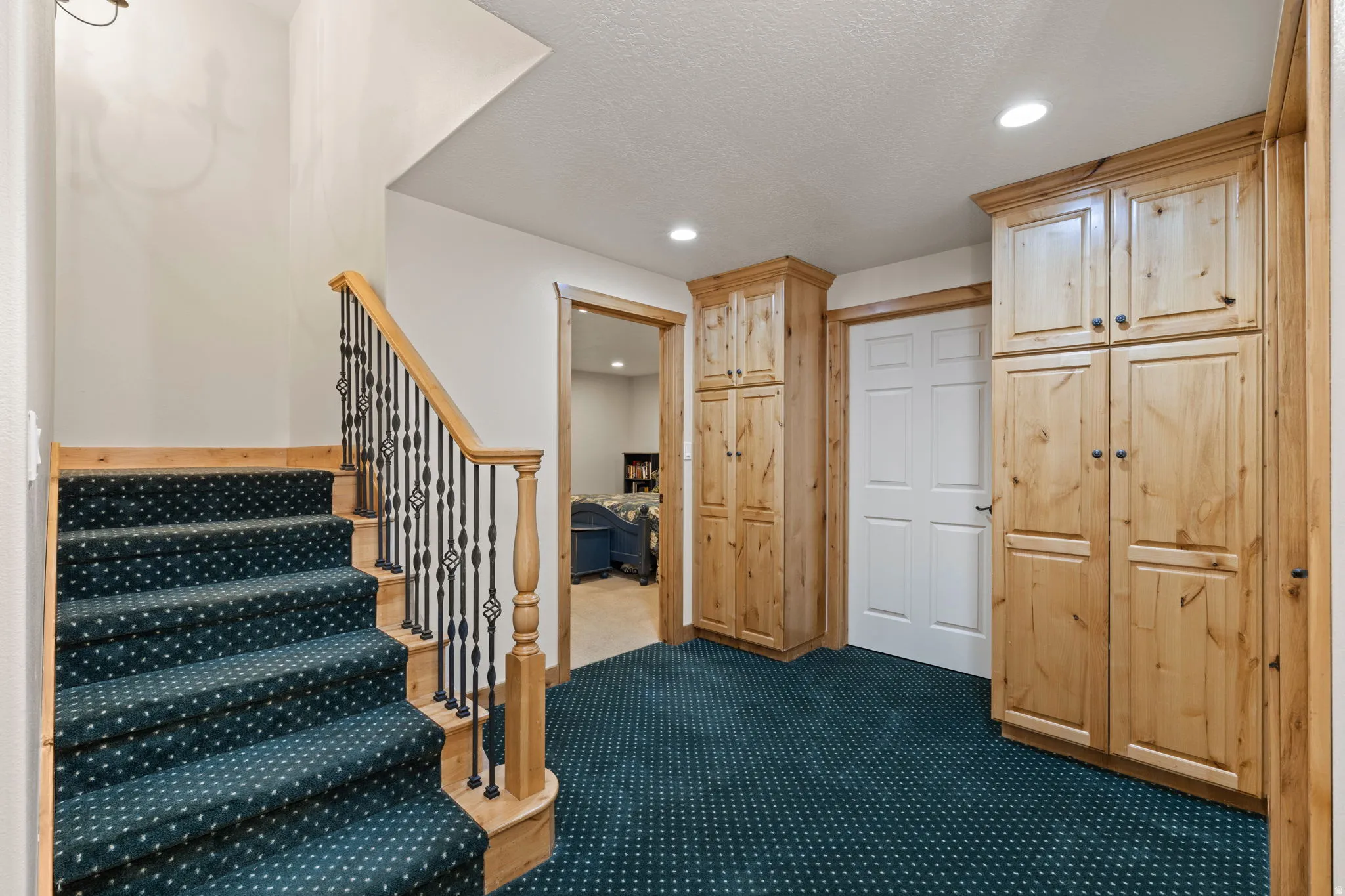Staircase with wood banister and wrought iron spindles, dark patterned carpeted treads, recessed lighting, and built-in wood cabinetry for storage