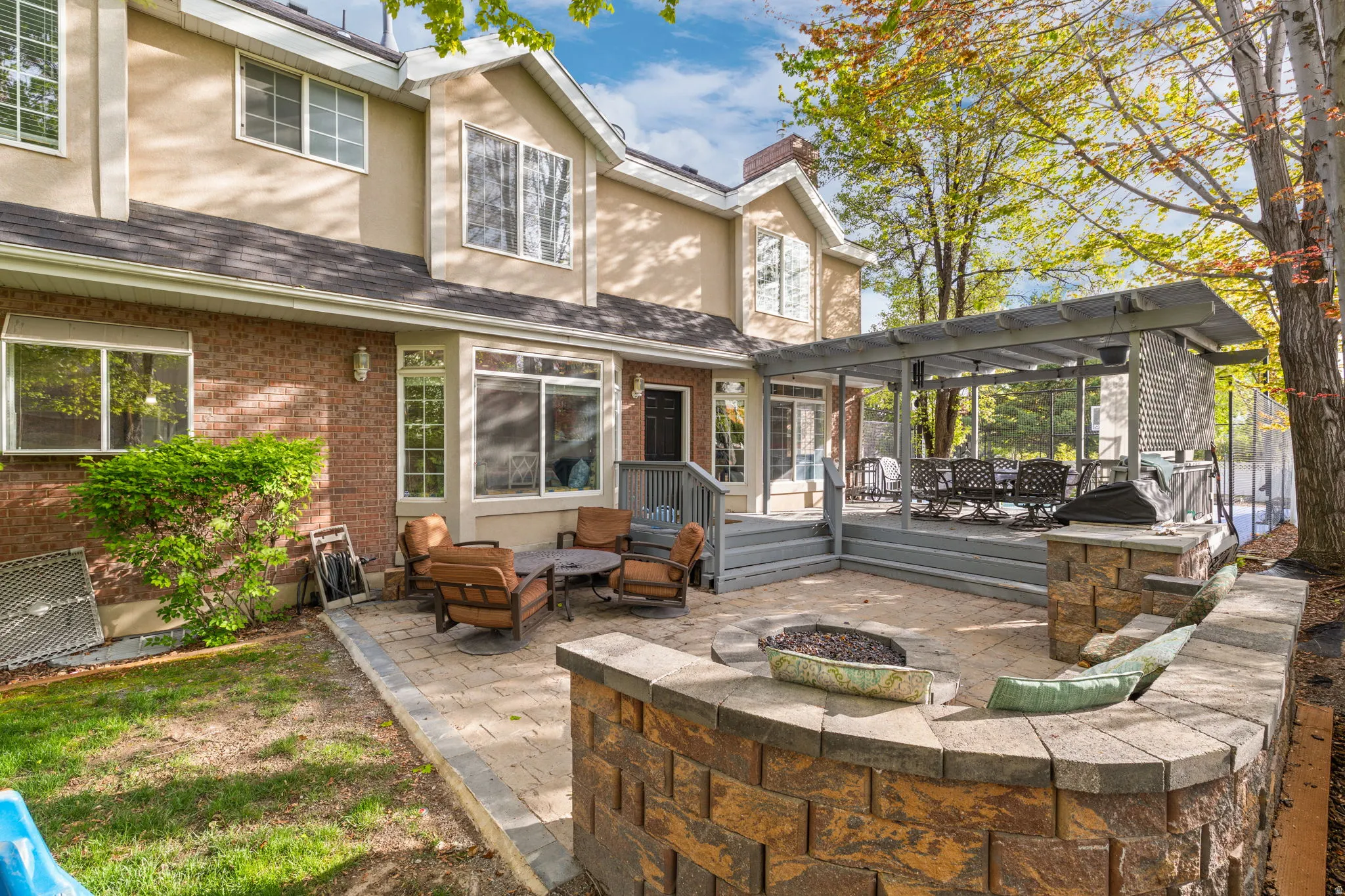 Expansive paver patio with a built-in fire pit, stone-clad retaining wall, and a multi-level wood deck