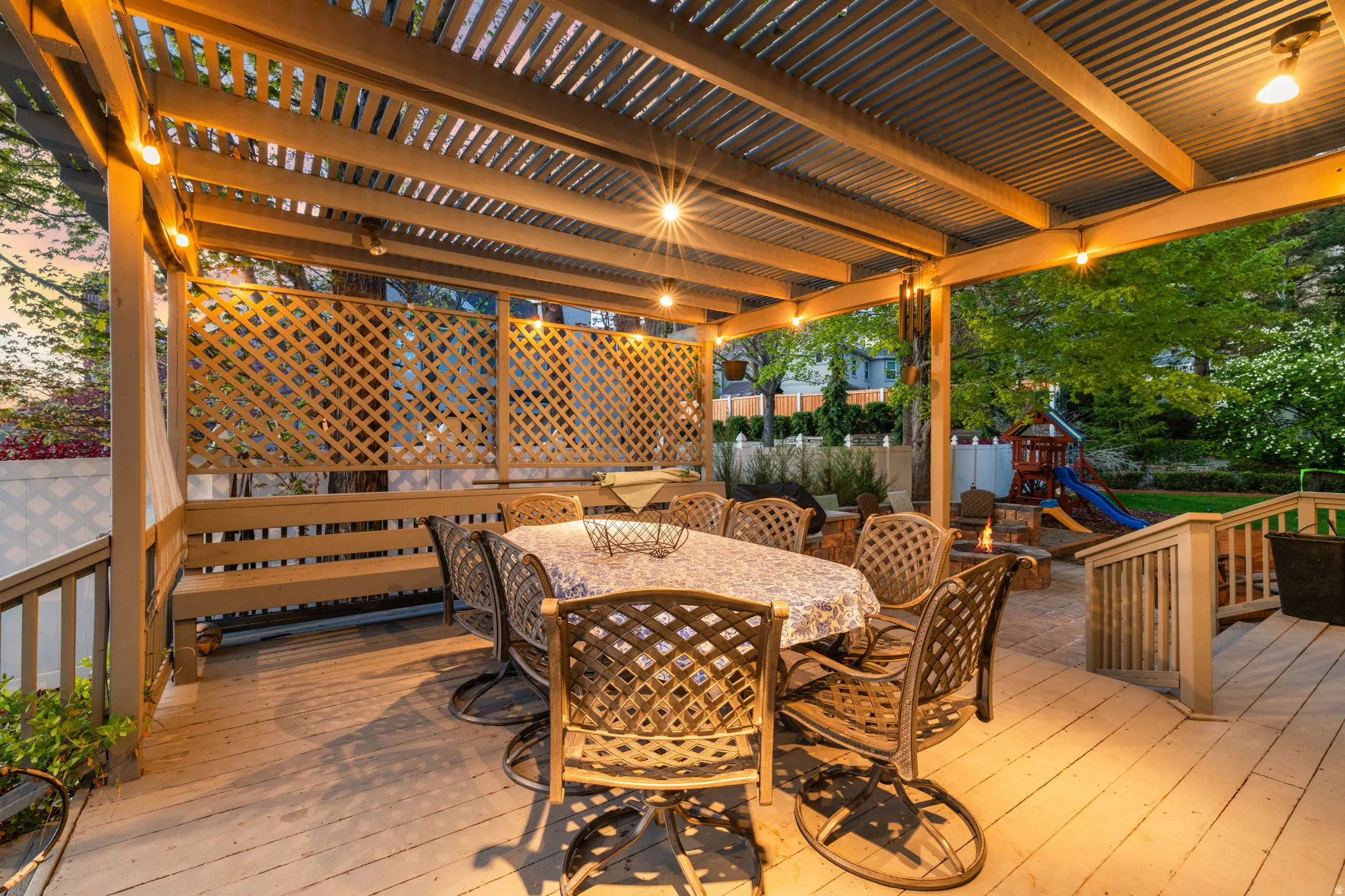 Wood-plank deck with a covered pergola featuring string lighting and a corrugated roof