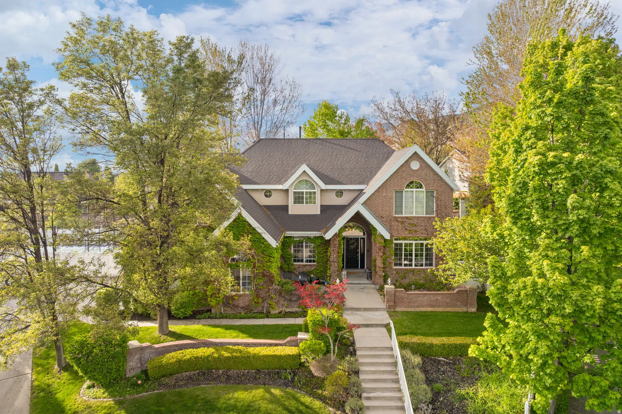 Brick and siding exterior featuring a multi-gable roofline, arched windows, and climbing ivy accents