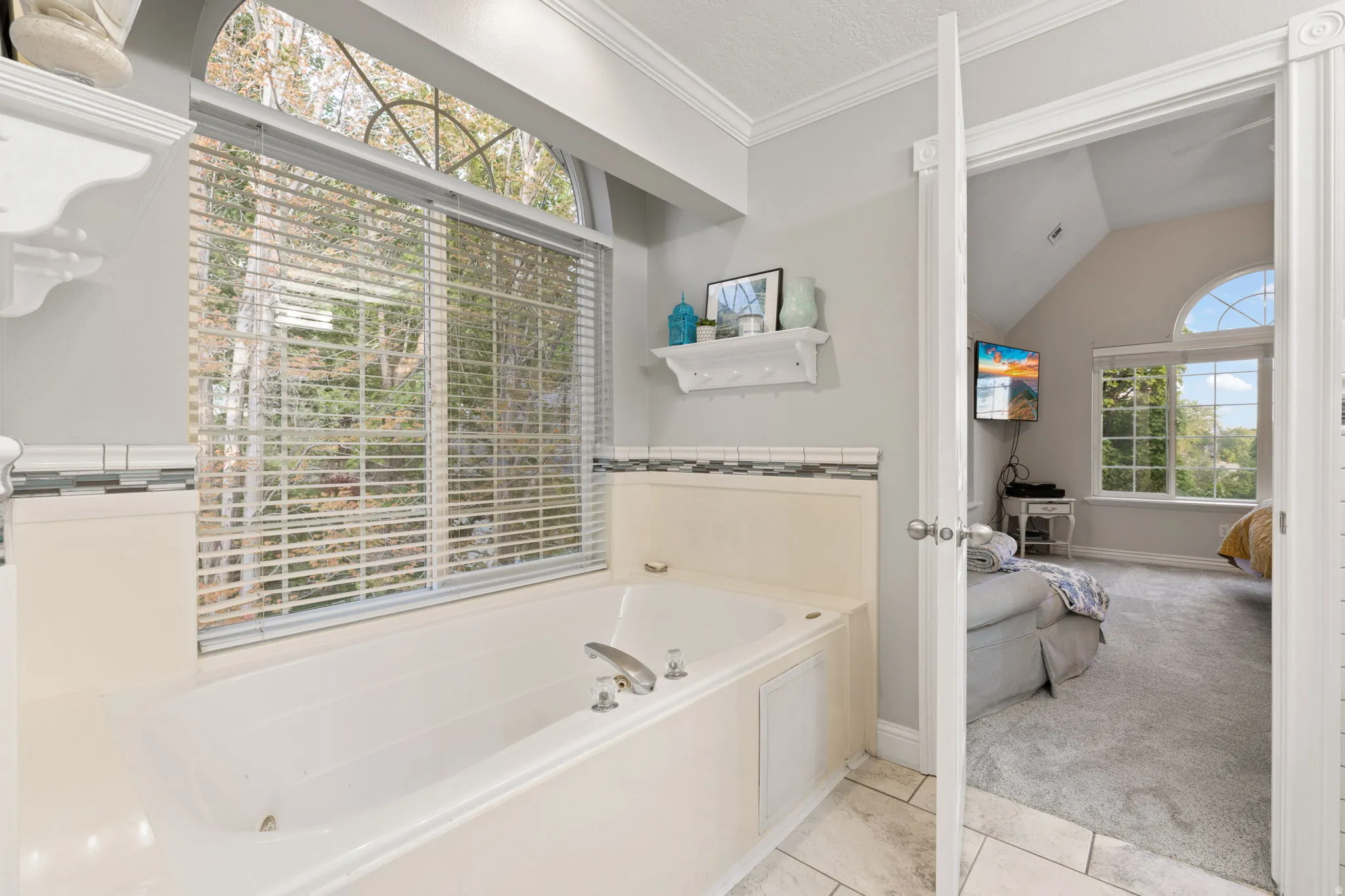 Primary bathroom with soaking tub set against a large window with arched transom