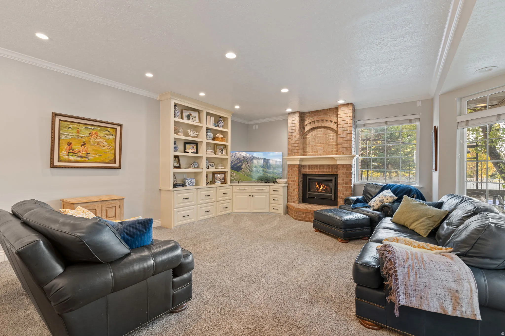 Brick fireplace with a raised hearth, recessed lighting, built-in cabinetry, custom shelving, and multiple window exposures