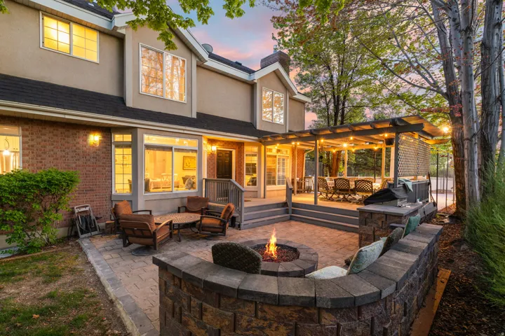 Spacious backyard featuring a paver patio with a built-in fire pit, stone-clad seating, and a covered outdoor deck