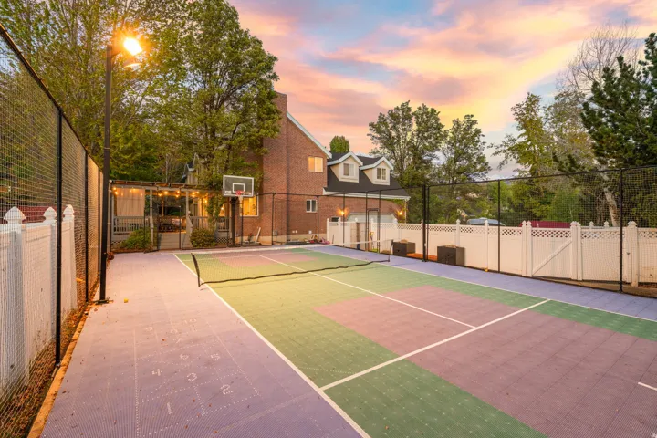 Multi-sport court featuring vibrant purple and green surfacing, integrated shuffleboard lines, a basketball hoop, and perimeter fencing