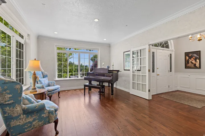 Spacious sitting room featuring wood-finish flooring, extensive window grid detailing, crown molding, and wainscoting