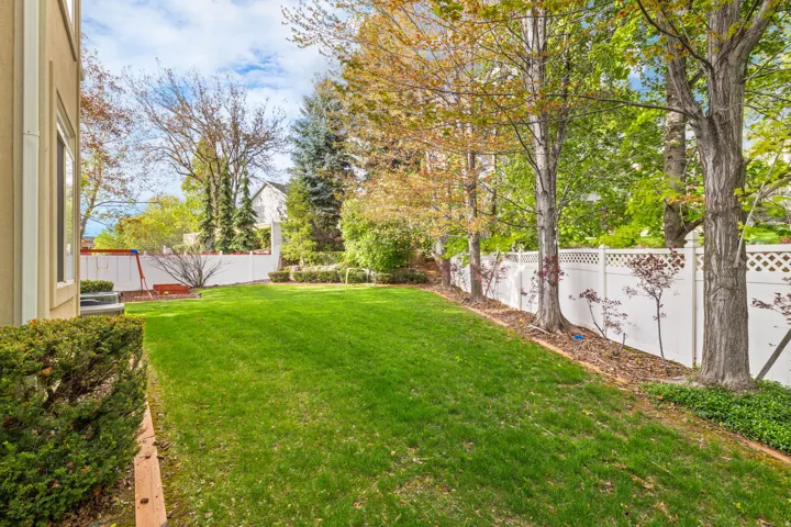 Expansive rear yard featuring a manicured lawn, established perimeter trees, and a white lattice-top privacy fence