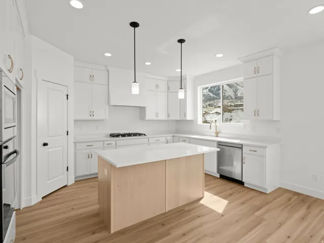 Modern kitchen featuring white cabinetry, a light wood-finish island with a white countertop, stainless steel appliances, and wood-finish flooring
