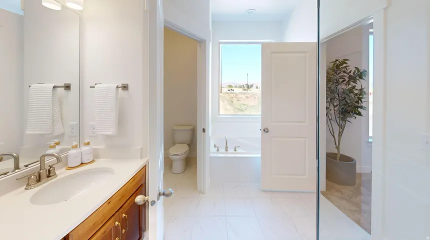Bathroom featuring a double vanity with wood-finish cabinetry and light-toned countertops, a built-in soaking tub, and white tile flooring