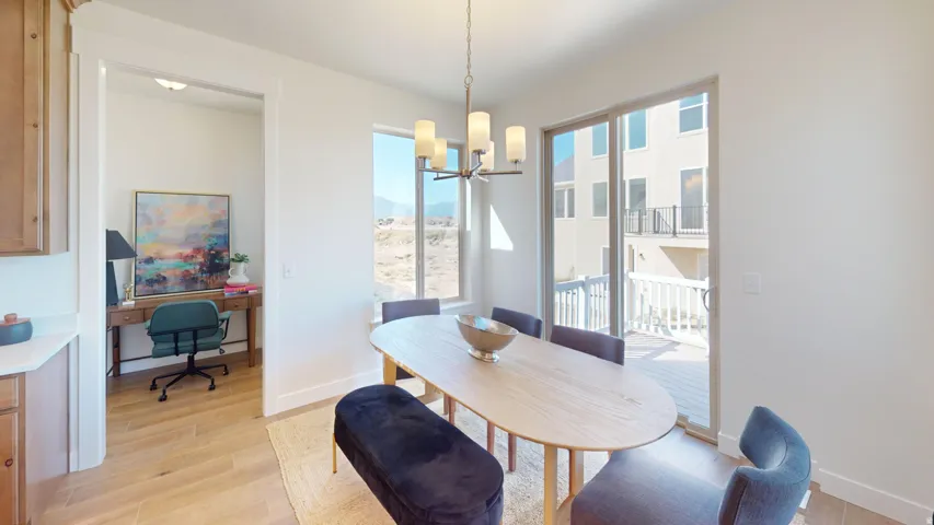 Open-concept dining area featuring light wood-finish flooring, a contemporary chandelier, and a sliding glass door leading to an outdoor deck