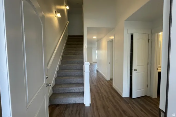 Entryway featuring wood-finish flooring, a carpeted staircase with white railing, and bright white walls