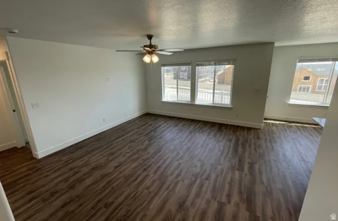 Spacious room featuring wood-finish flooring, multiple windows providing natural light, a ceiling fan with integrated lighting, and white baseboards